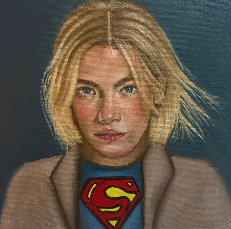 Oil portrait of a young woman with a blonde bob in a tan coat over a blue top with a red and yellow emblem, 15 × 15 in